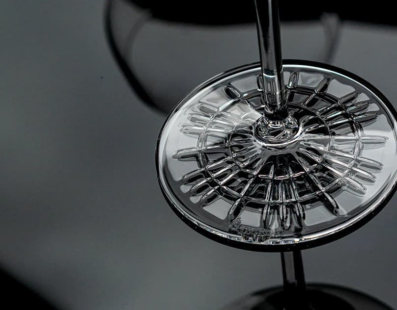 The cut-crystal foot and stem of a wine glass photographed from below against grey.