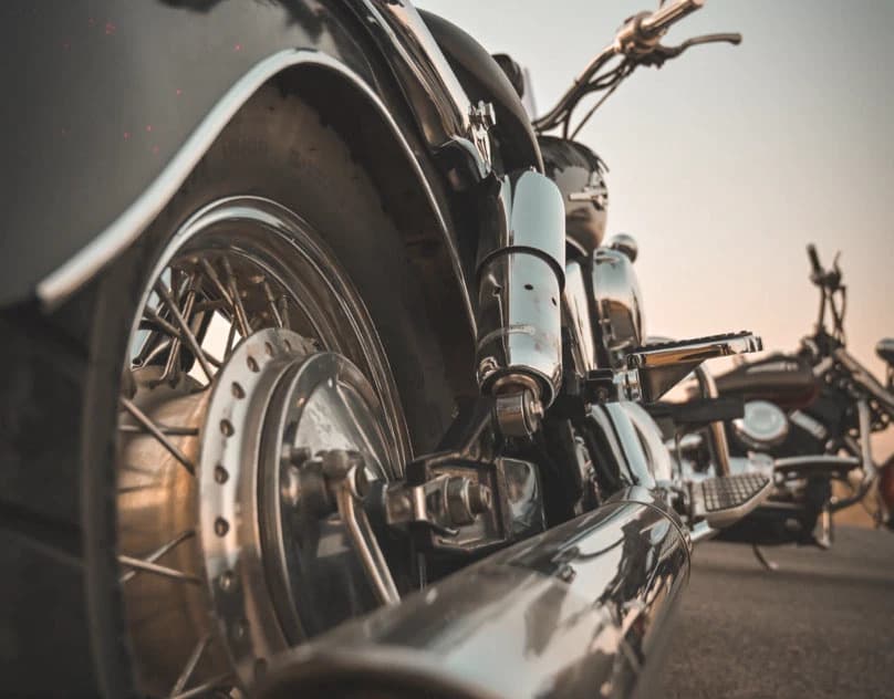 A low close view along a chrome cruiser motorcycle at dusk, with a second bike behind it.