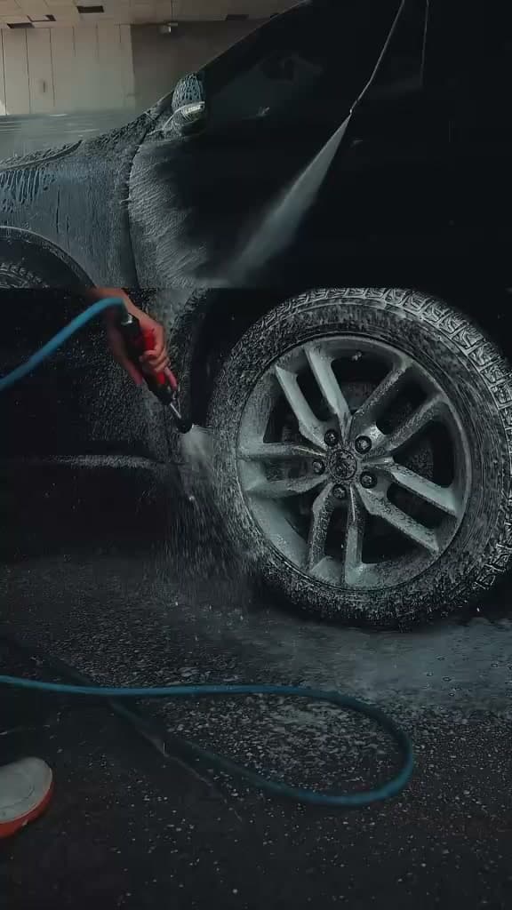 Vertical short film showing a black car being cleaned with foam and a pressure washer.