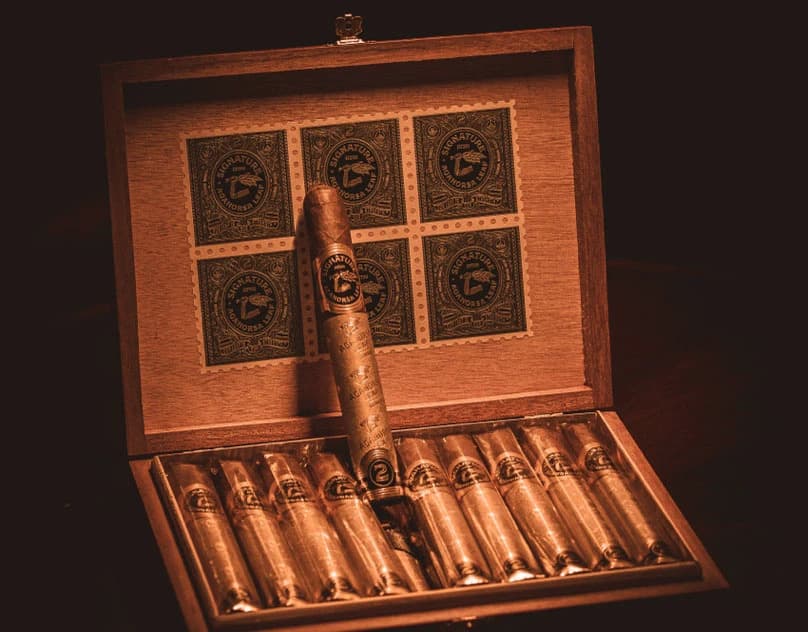 An open wooden cigar box with one cigar resting across wrapped rows in warm light.