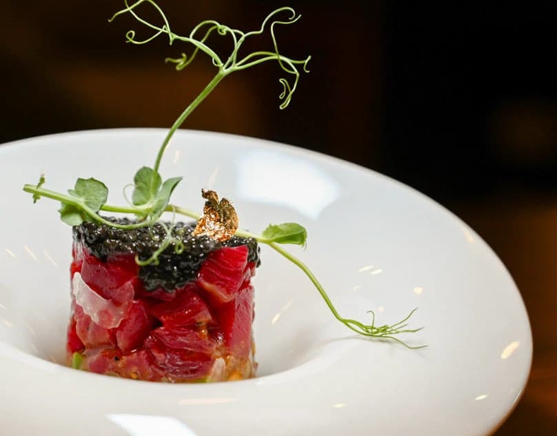 A tuna tartare timbale topped with caviar and pea shoots in a white bowl.